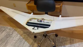 Walkaround of the white flying wing on a chair indoors, moving in on the open center bay's wiring, circuit boards and mounting strips