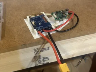 Matek F405-WING V2 flight controller and a small green circuit board on a white 3D-printed tray, with red and black power leads