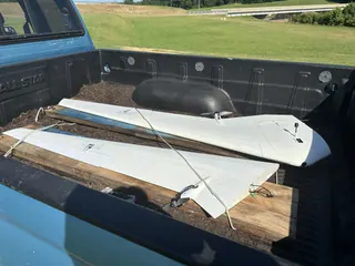 White flying wing split into two halves, tied down on boards in a pickup bed; one root end shows wires and yellow connectors