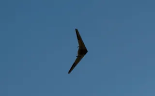 Flying wing seen from below in flight, a dark silhouette against a clear blue sky with two motor pods visible