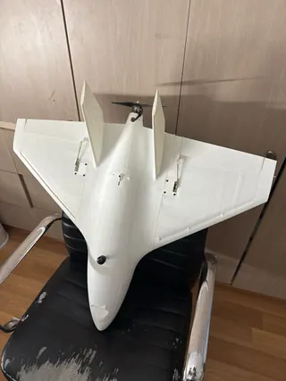 Top-down view of a white 3D-printed jet-style delta with twin canted fins and a rear propeller, resting on a black office chair
