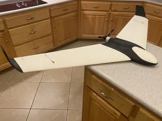 Swept flying wing with cream wing panels, black center body and black winglets, and a rear propeller, resting on a kitchen counter